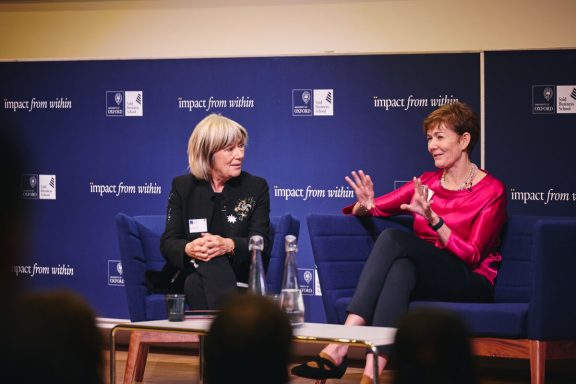 Two women seated on stage engaged in discussion, with an attentive audience visible.