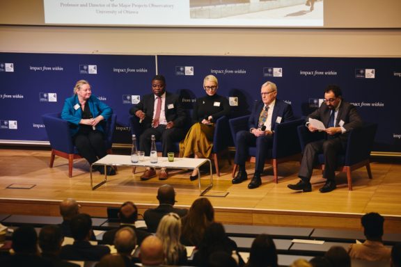 A panel discussion featuring five speakers on stage, with an audience visible.