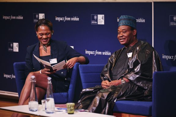 Two people seated, engaged in discussion, one in traditional attire, smiling and interacting.