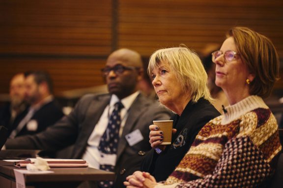 Three people attentively listening during a presentation, with a coffee cup in hand.